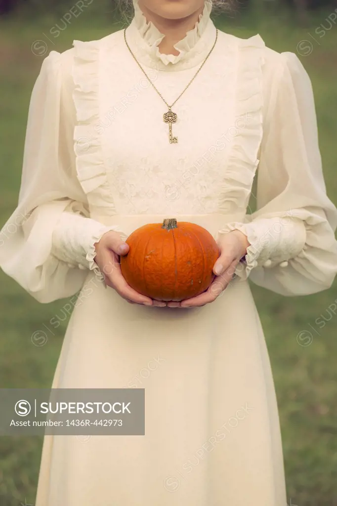 a woman in a victorian dress is holding a pumpkin