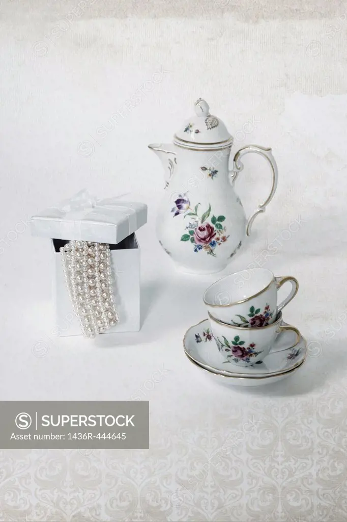 two vintage coffee cups, a coffee pot and a present box with a pearl necklace