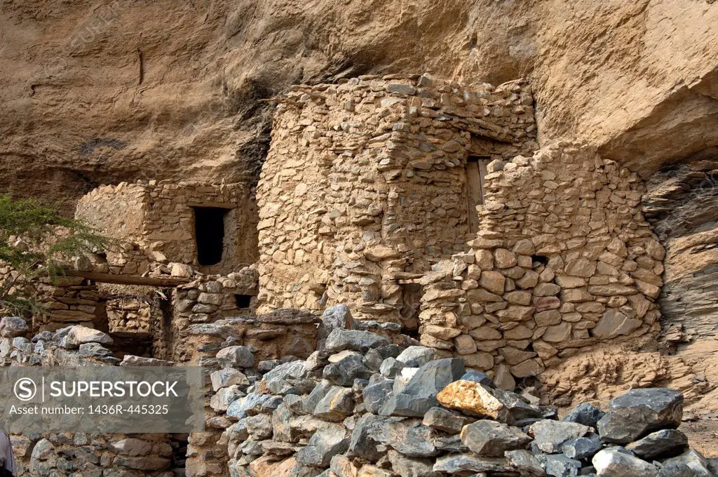 Stone huts of the deserted village of Sap Bani Khamis under a rock overhang in the Grand Canyon of Oman in Wadi an Nakhur, Jabal Akhdar mountains, Sul...