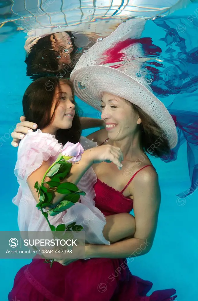 Woman and girl, underwater models, presenting fashion in pool