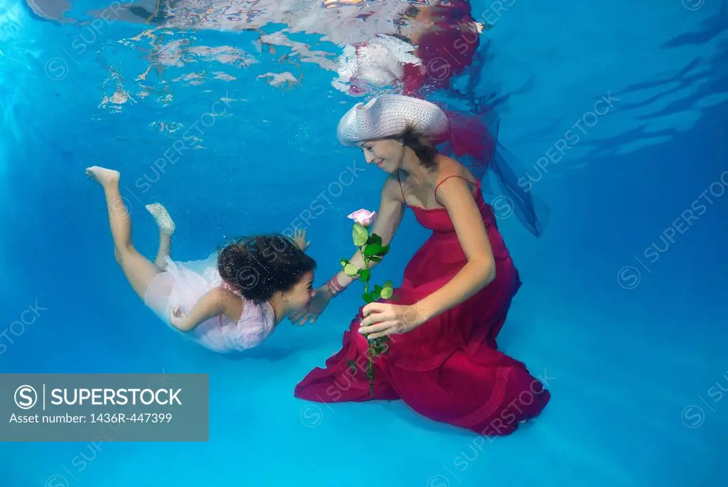 Woman and girl, underwater models, presenting fashion in pool