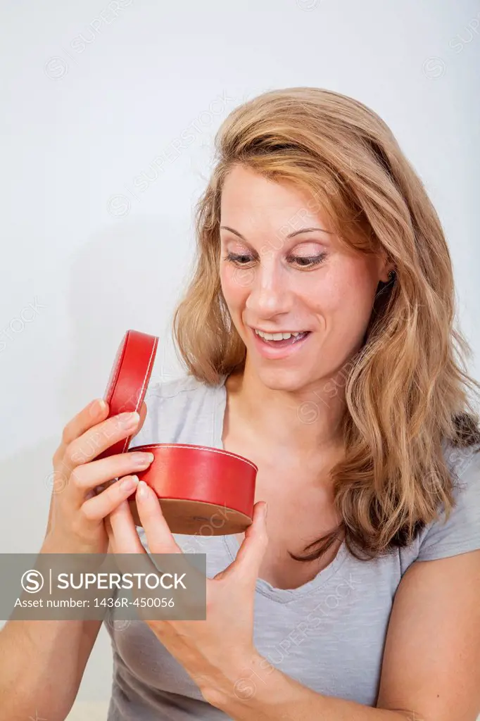 Young woman looking inside a round red container.