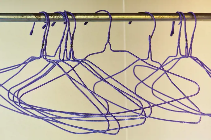 Group of empty purple wire coat hangers hanging on rail.