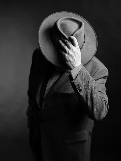 Male wearing dark suit and he covering face with a hat, black and white image.