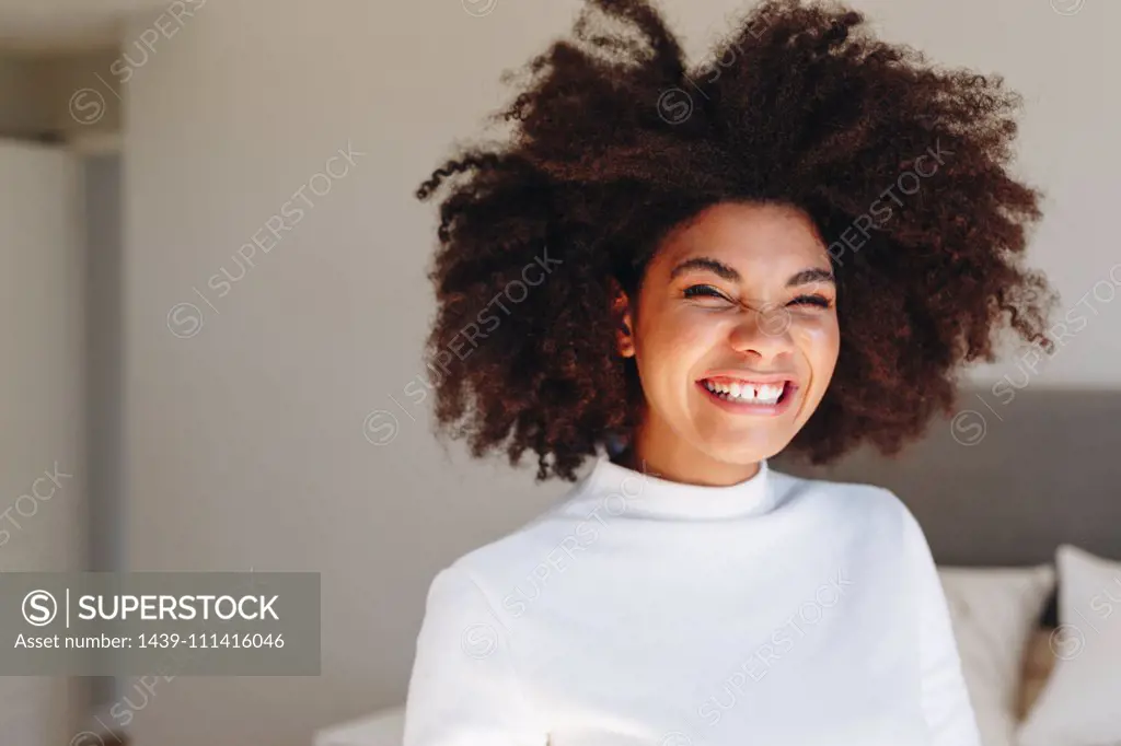 Young woman with afro hairstyle laughing in bedroom, head and shoulder portrait