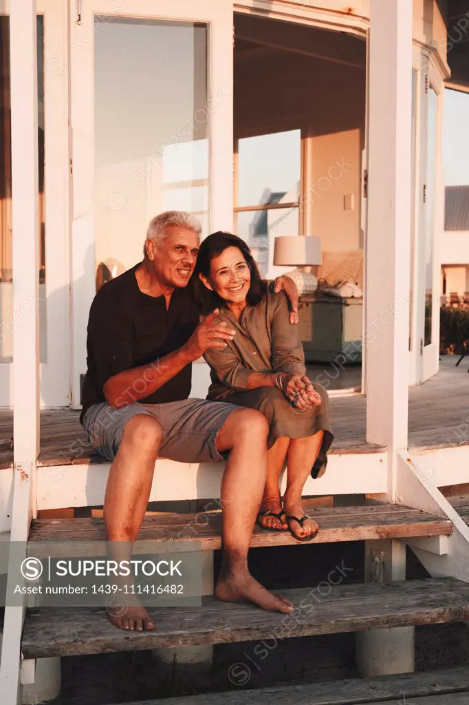 Senior couple enjoying sunset on steps in front of beach house