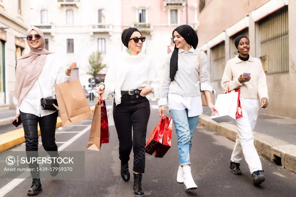 Four female friends walking along street with shopping bags