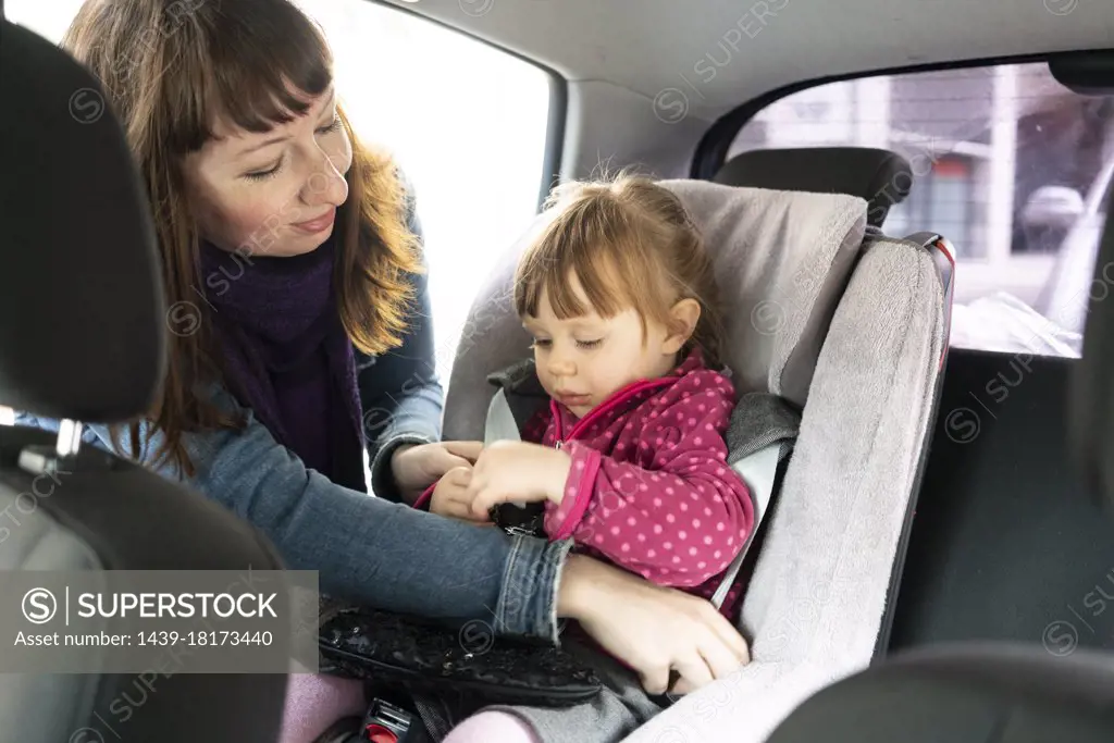 Mother putting daughter into car seat