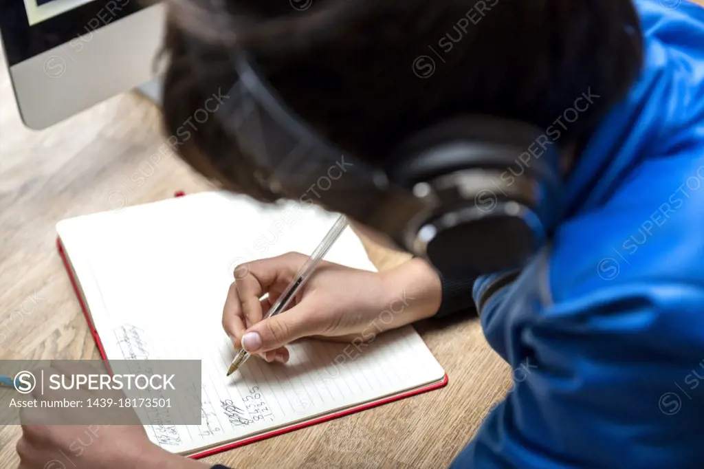 UK, Boy in headphones writing in notebook