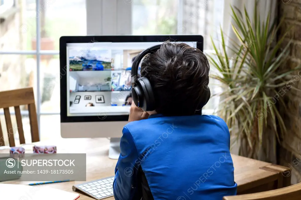 UK, Rear view of boy with headphones sitting in front of computer