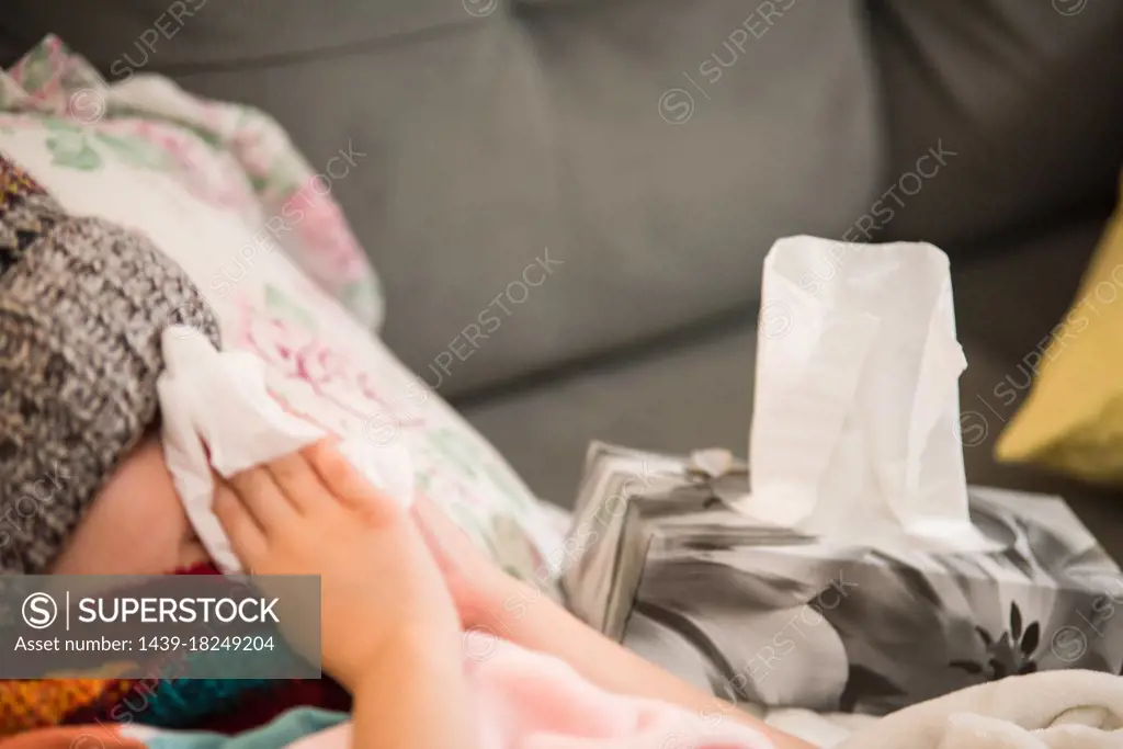 Canada, Ontario, Boy (8-9) in knit hat blowing nose on sofa
