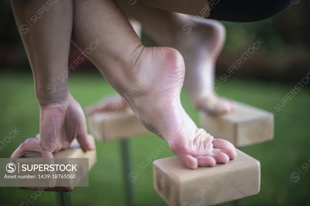 Close-up of foot and hand of female gymnast balancing on blocks outdoors