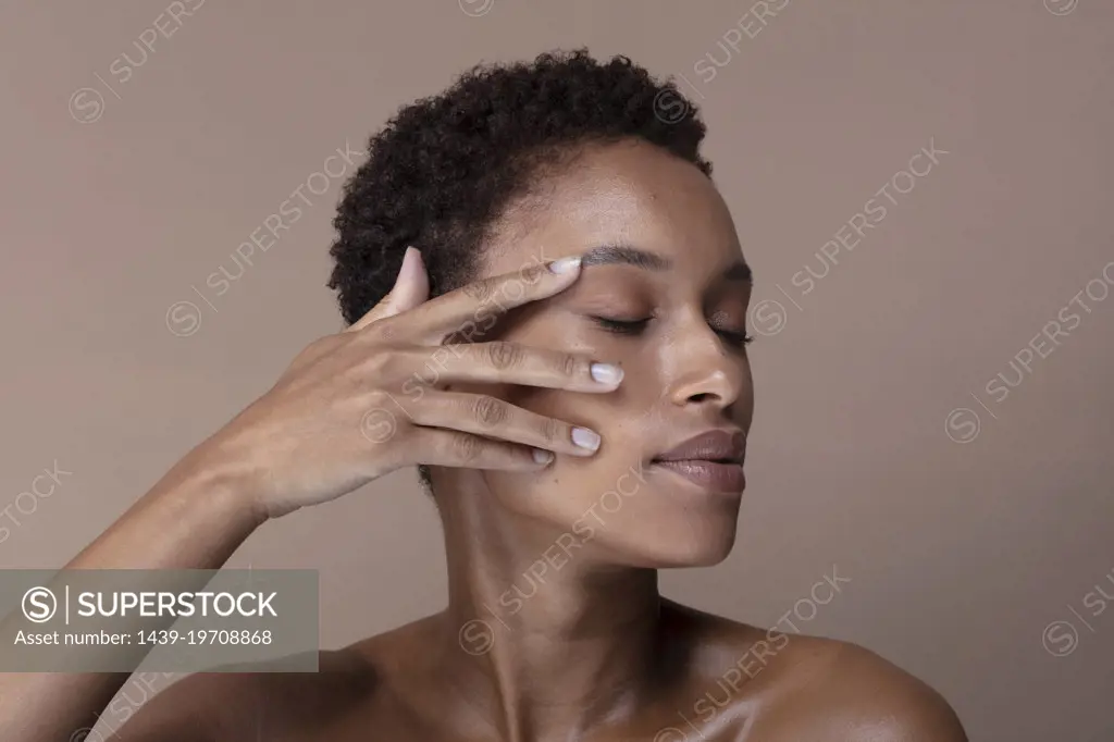 Studio shot of woman with eyes closed touching face