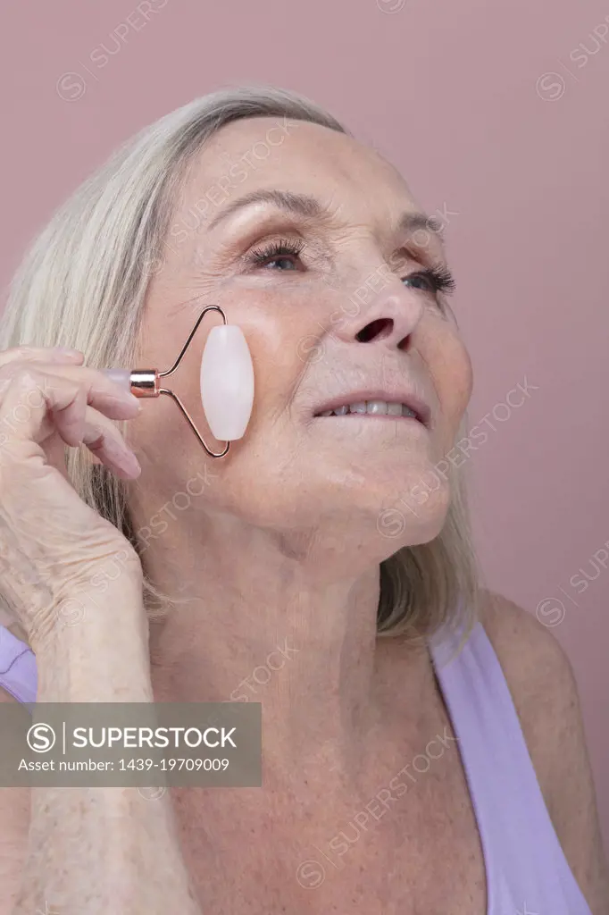 Studio shot of senior woman using face roller
