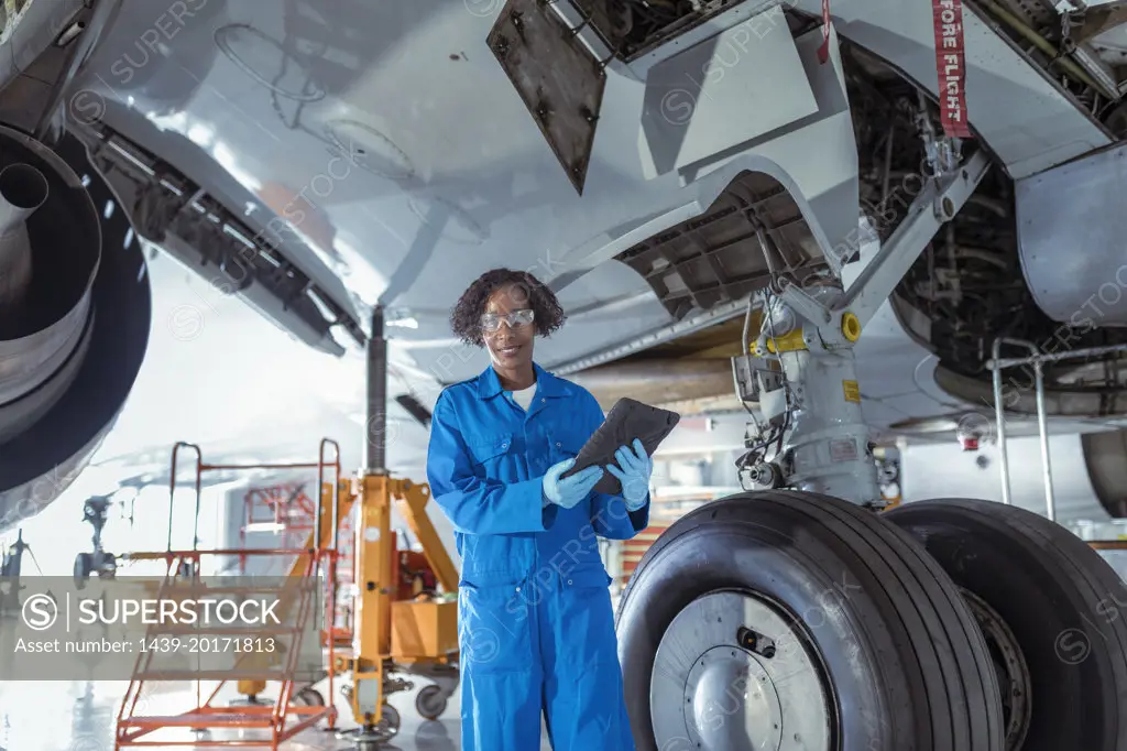 Female aircraft maintenance engineer underneath jet with digital tablet