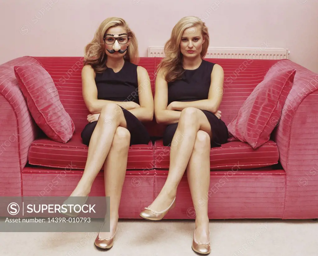 Two women on a sofa one wearing a comedy disguise