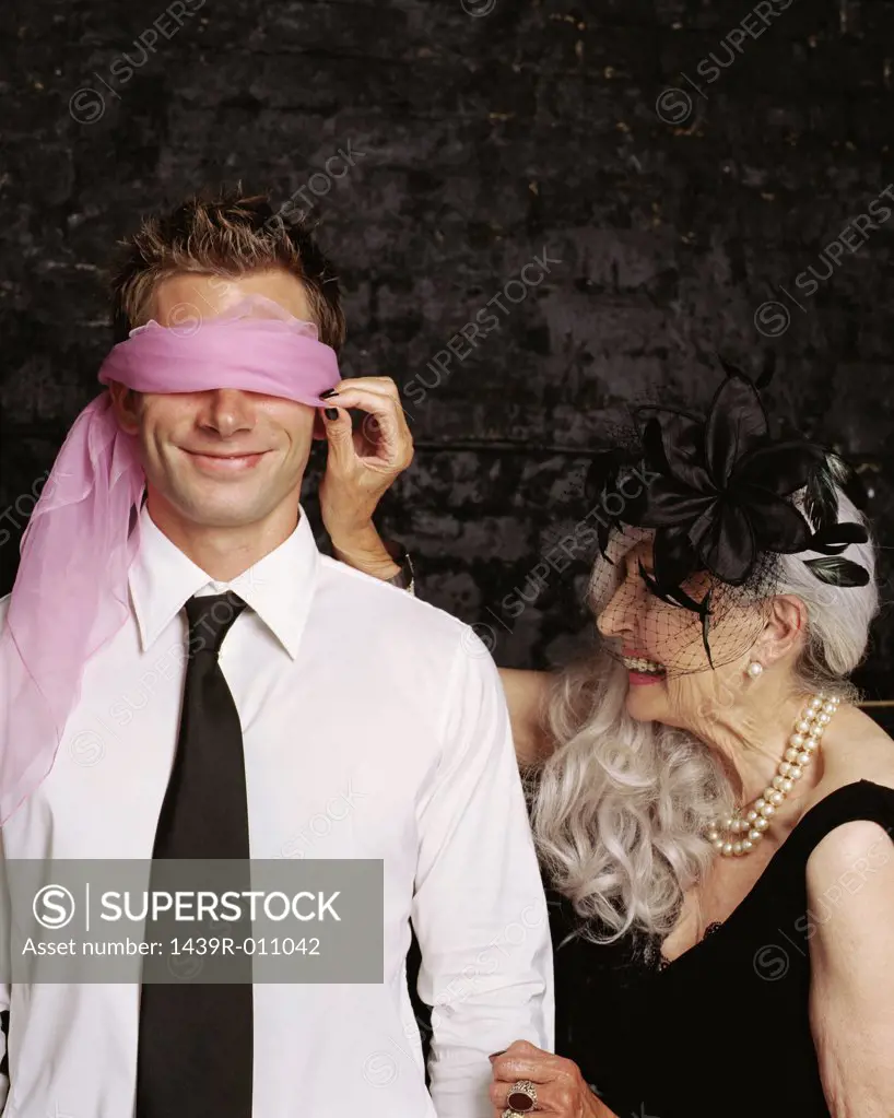 Senior adult woman adjusting scarf covering young adult man's eyes