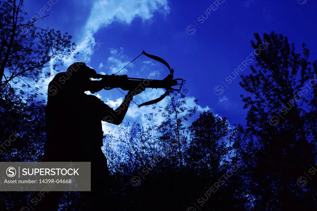 Silhouetted man aiming crossbow