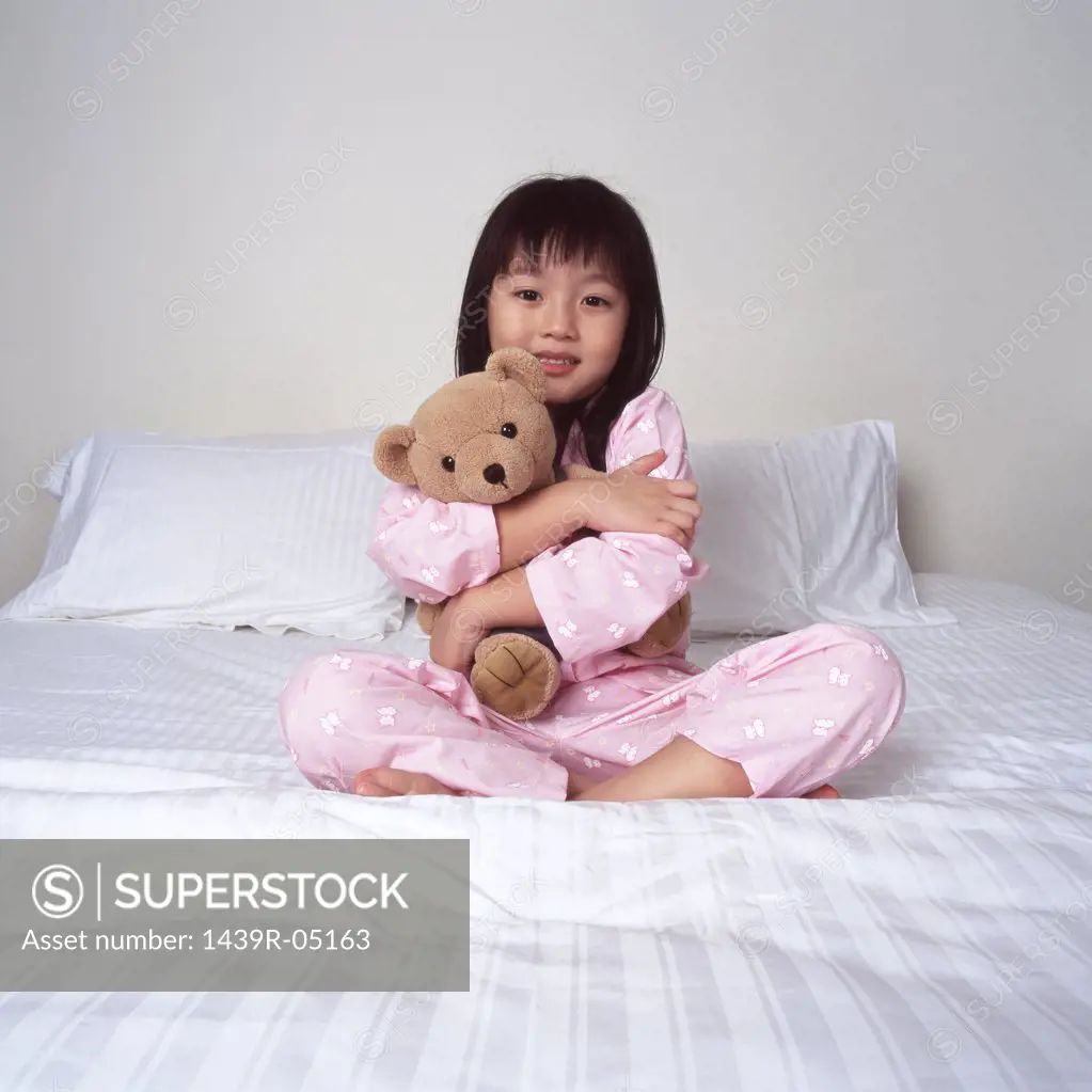 Young girl cuddling bear on bed