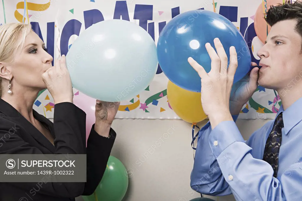 Two office workers blowing up balloons