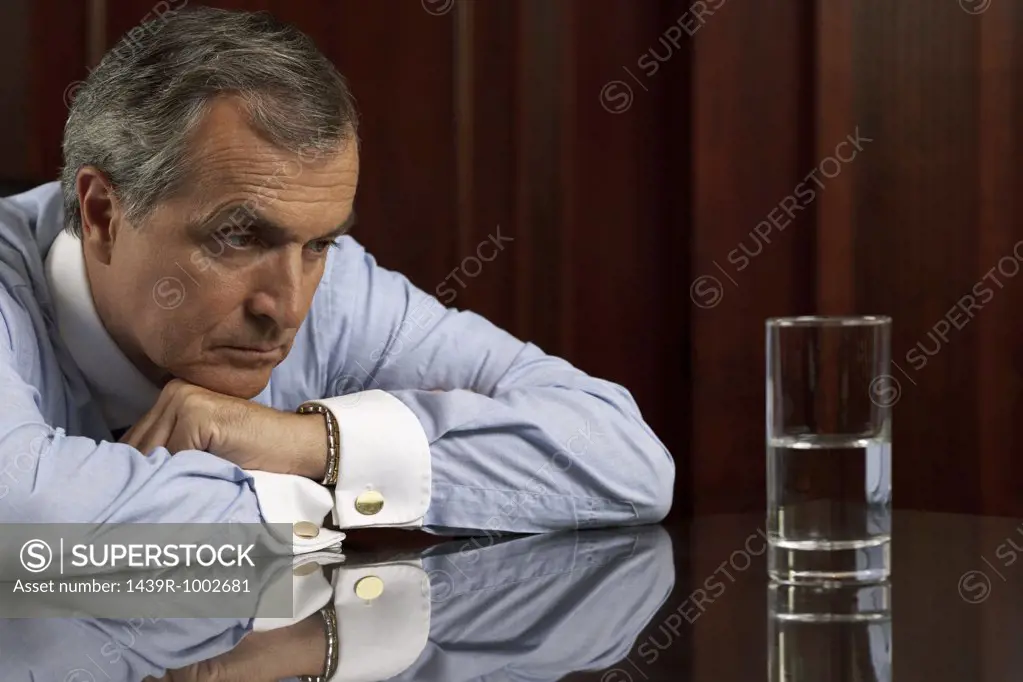 Businessman looking pessimistically at a glass of water