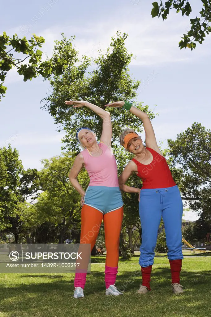 Two senior adult women stretching in park