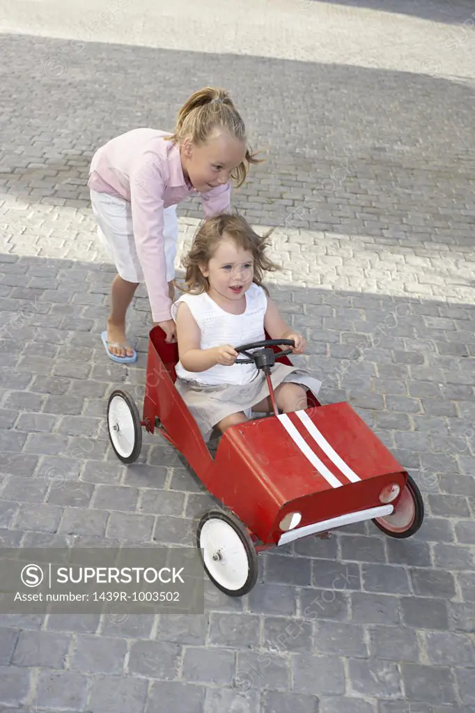 Sister pushing her younger sister in a toy car
