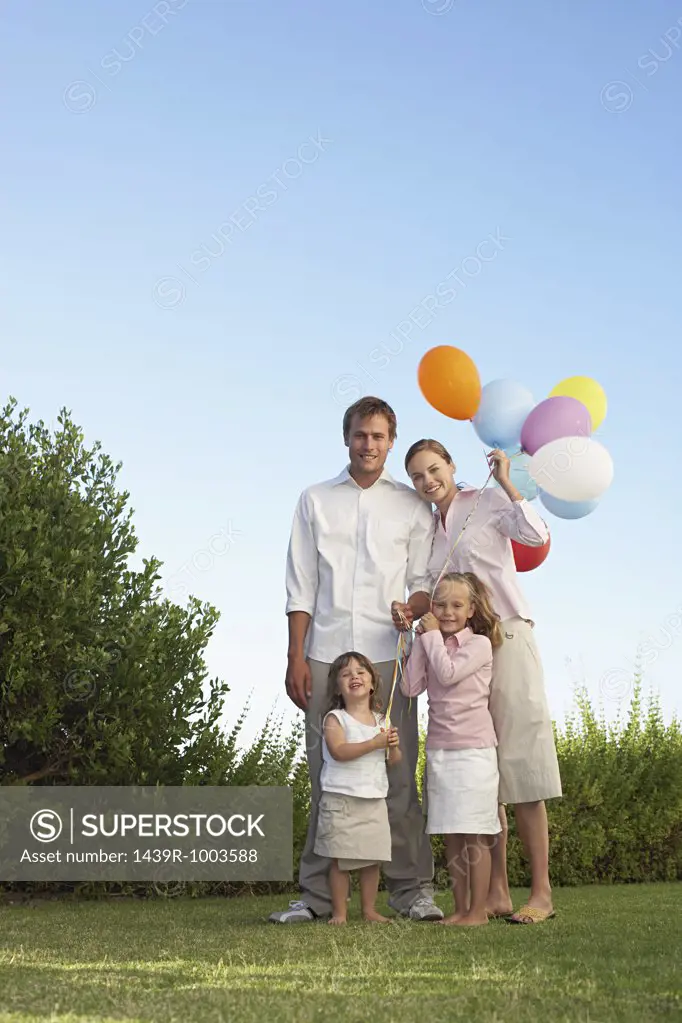 Portrait of family stood in garden with balloons