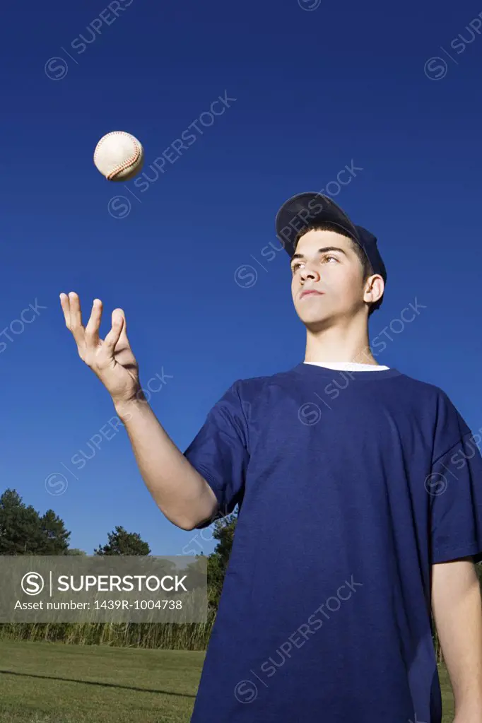 Teenage boy throwing baseball in the air