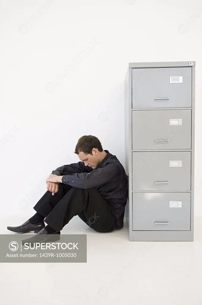 Businessman hiding behind filing cabinet