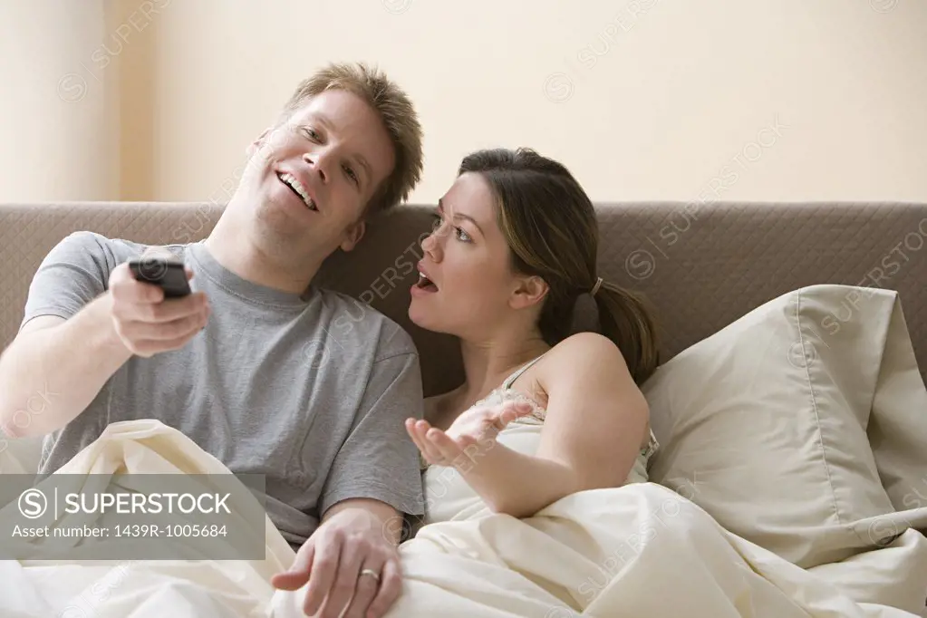 Couple watching television and arguing in bed
