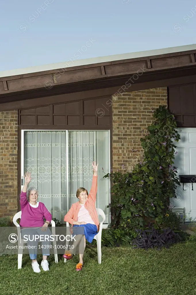 Two senior women sat in garden waving