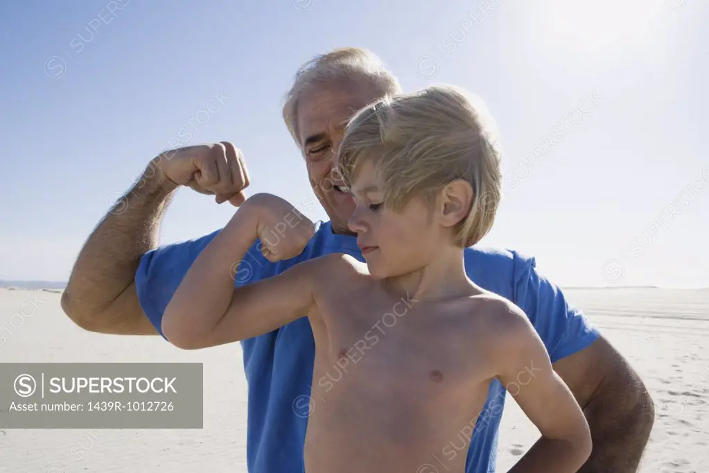 Grandfather and grandson flexing biceps on beach
