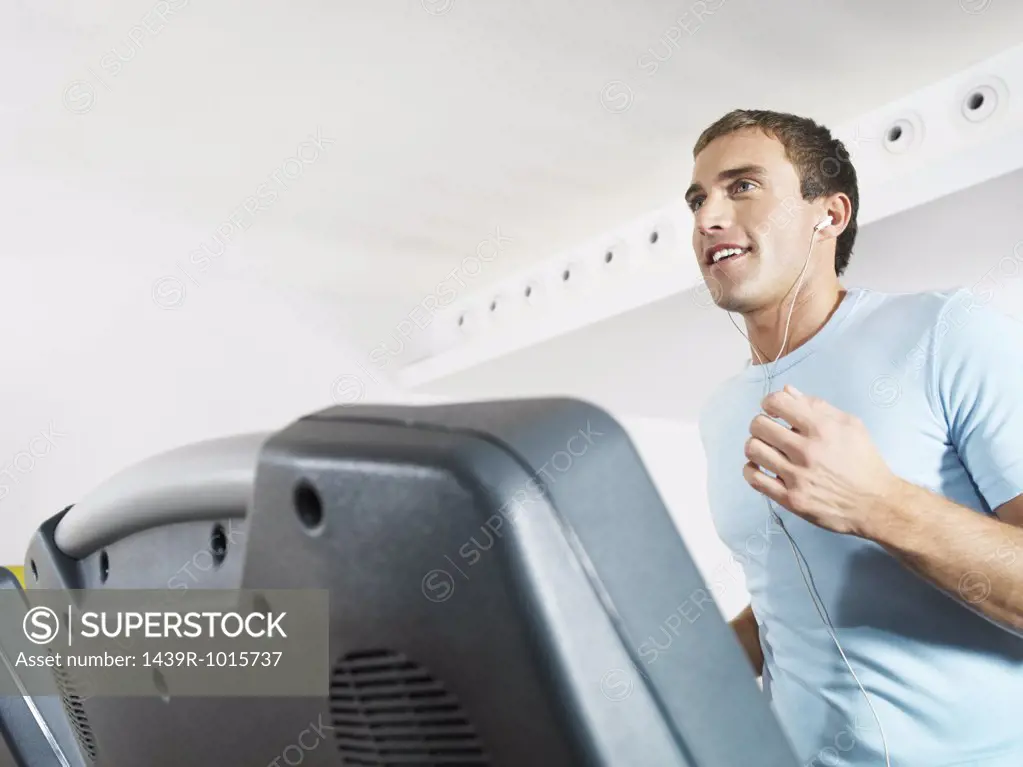 Man wearing earphones on treadmill in health club 