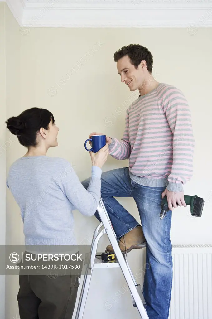 Woman handing coffee to husband on stepladder