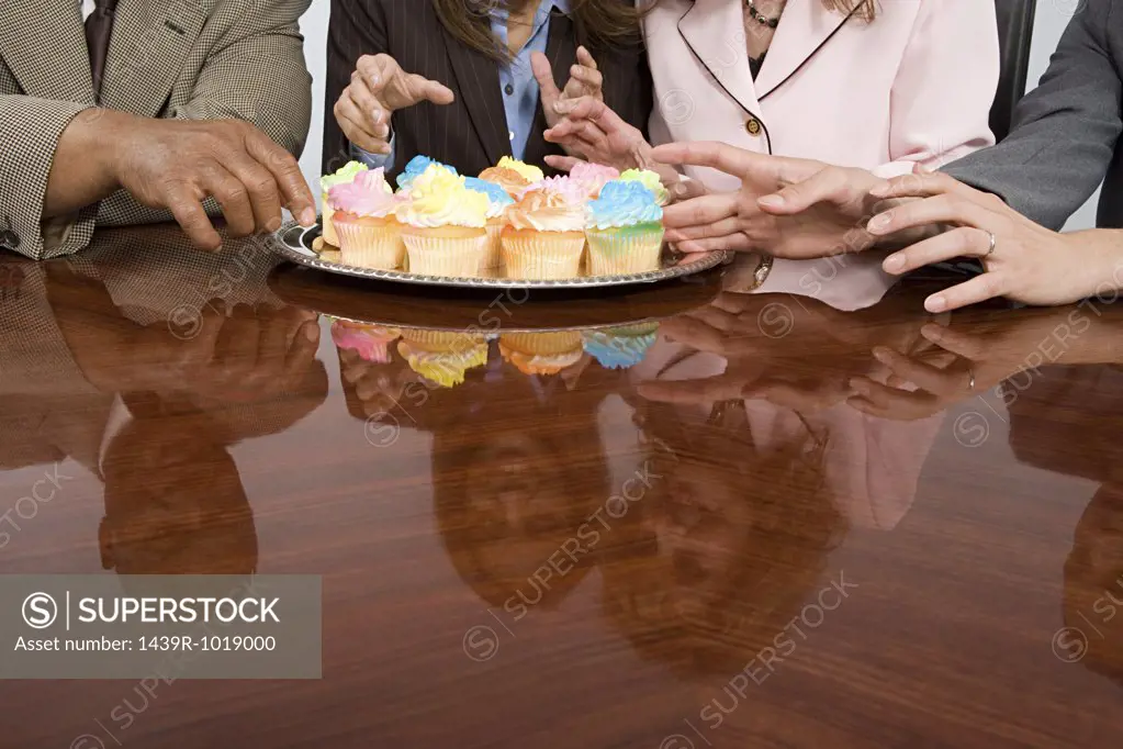 Businesspeople reaching for cupcakes
