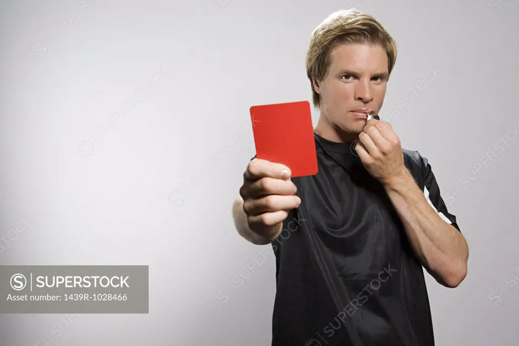 Referee holding red card and blowing whistle