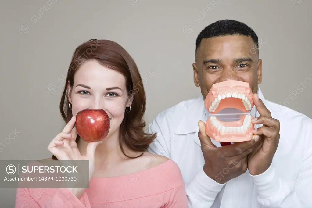 Dentist and woman holding an apple and false teeth