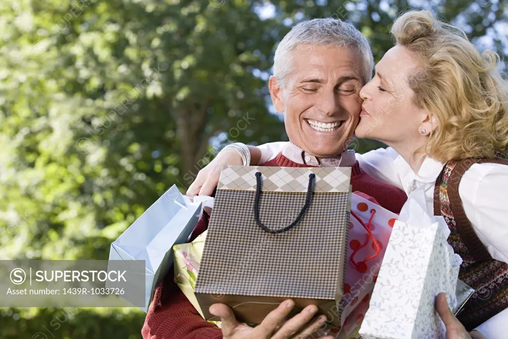 Wife kissing husband with bags of gifts