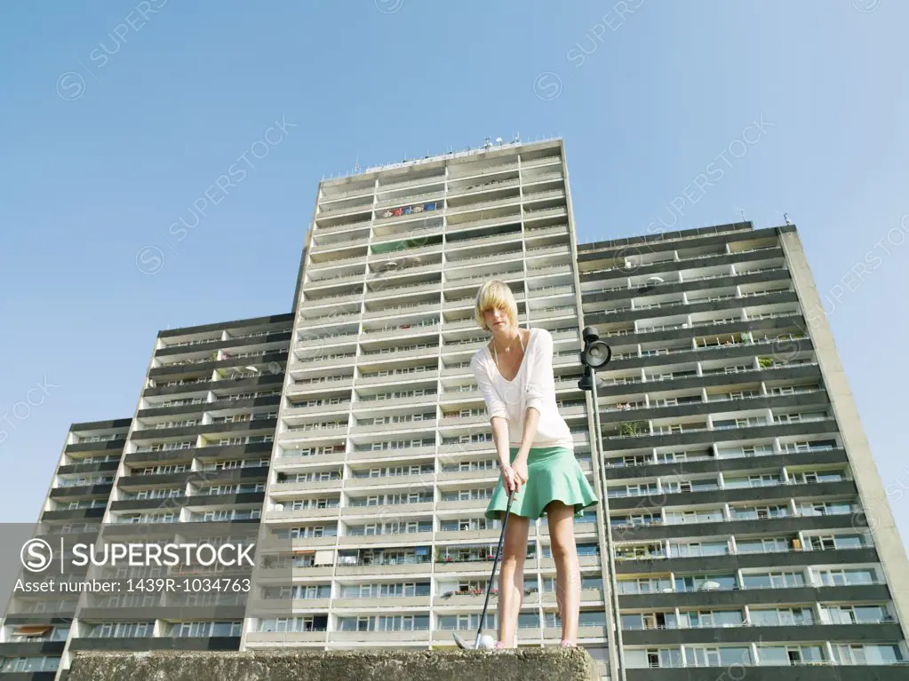 Woman playing golf by apartment block