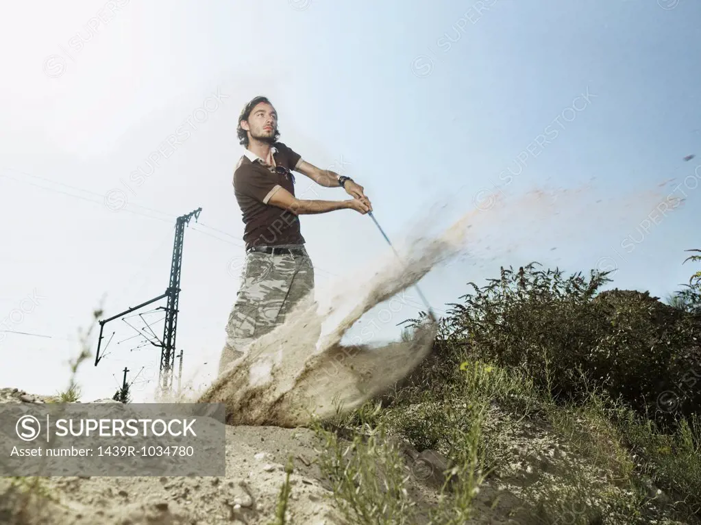 Young man playing golf on wasteland