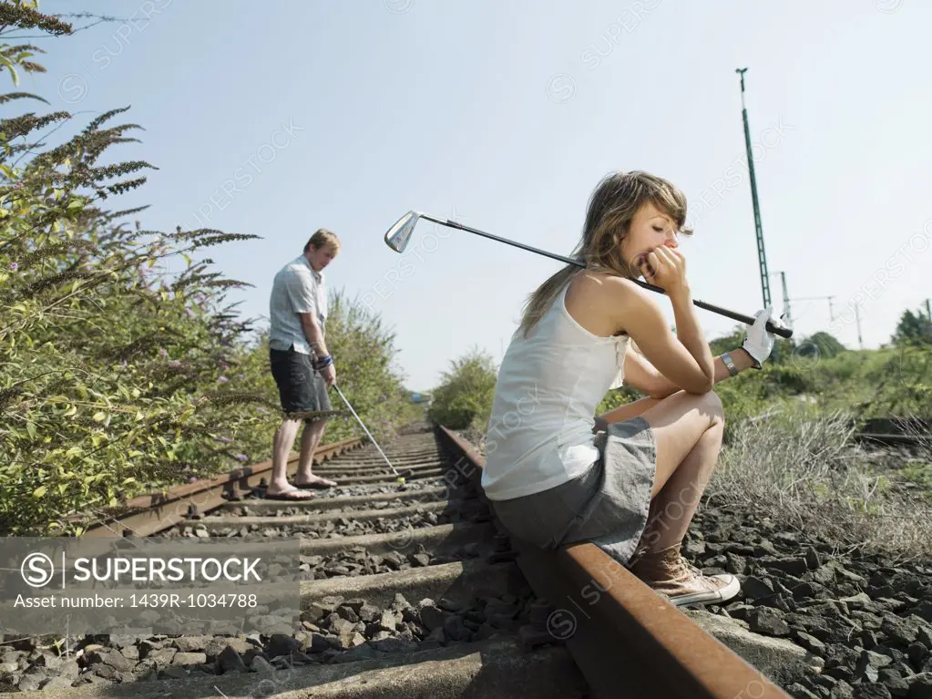 Man on woman playing golf on railway track