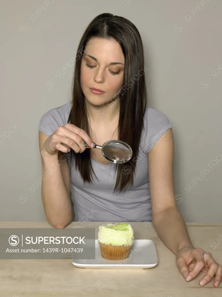 Young woman looking at cake with magnifying glass