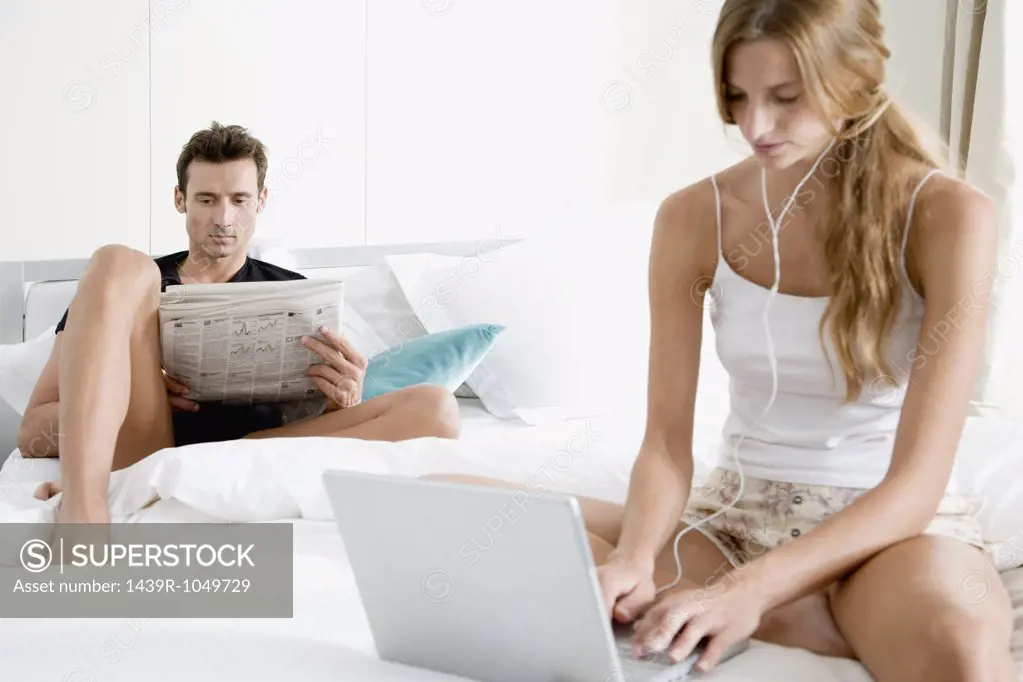 Couple on bed with newspaper and laptop