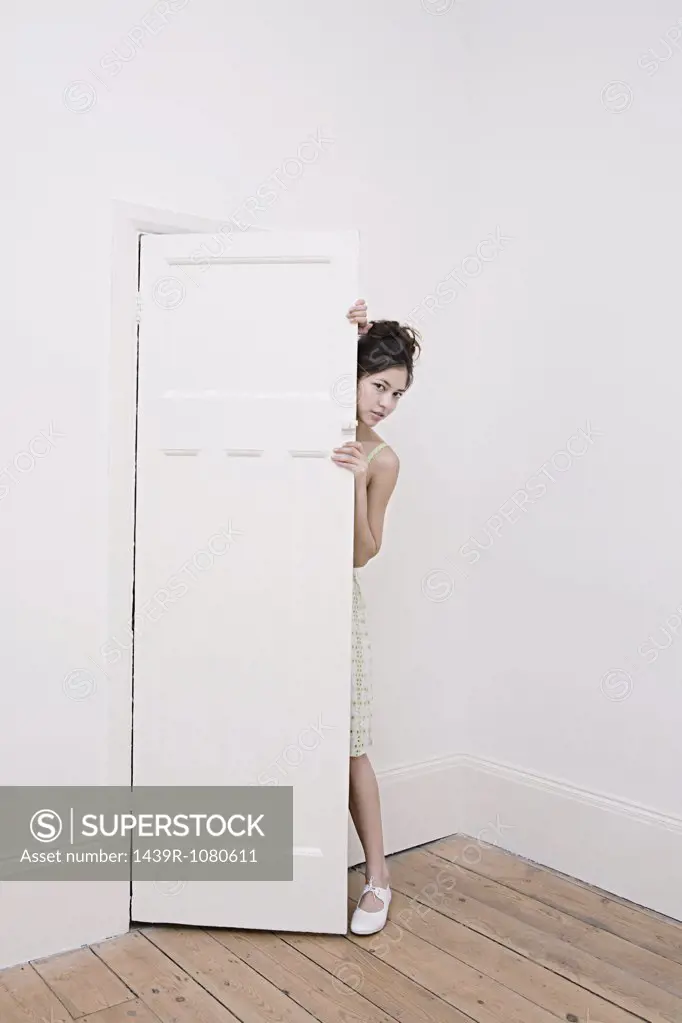 Young woman hiding behind a door