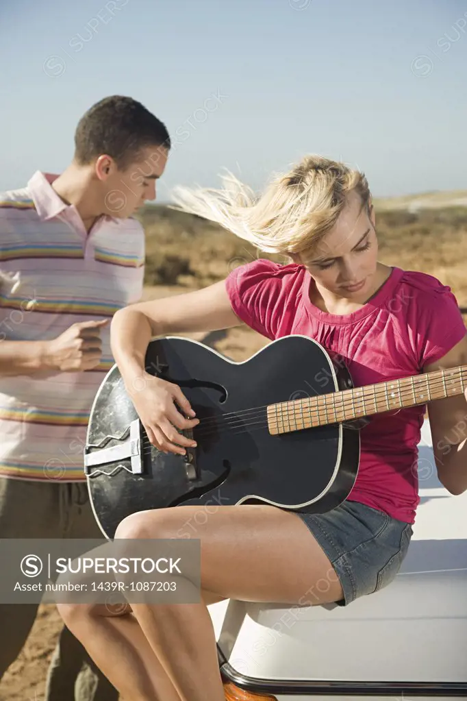 A young woman playing a guitar and a young man