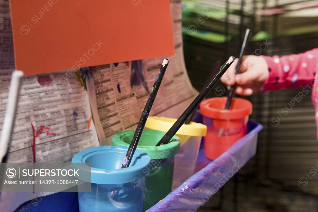 A girl putting a paintbrush in a paint pot