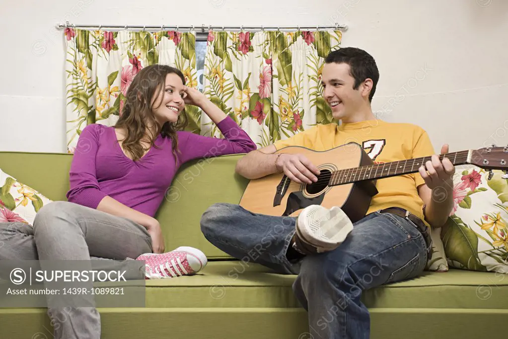 A teenage boy playing a guitar for a teenage girl