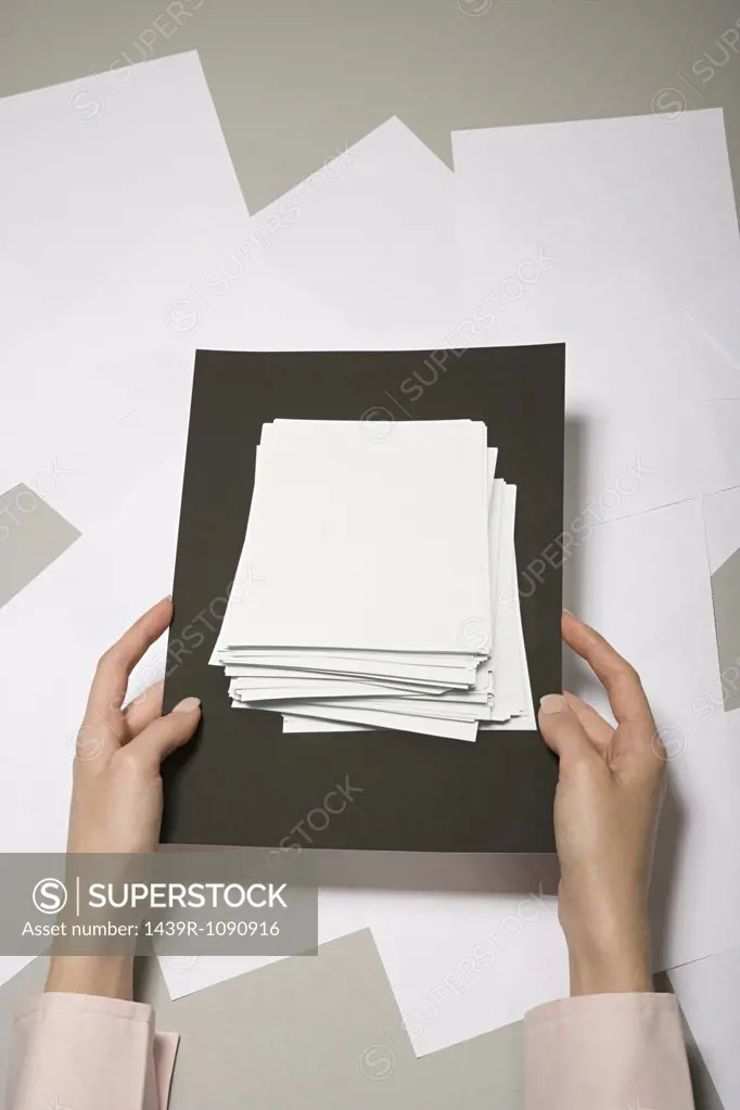 A woman holding a photograph of a stack of paper