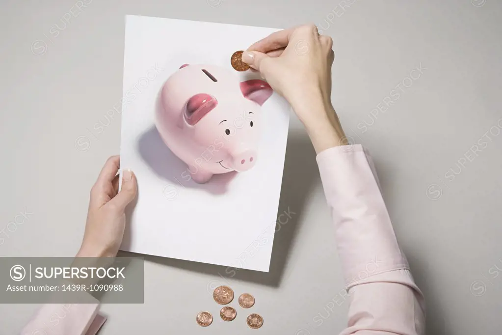 A woman holding a photograph of a piggy bank and a coin